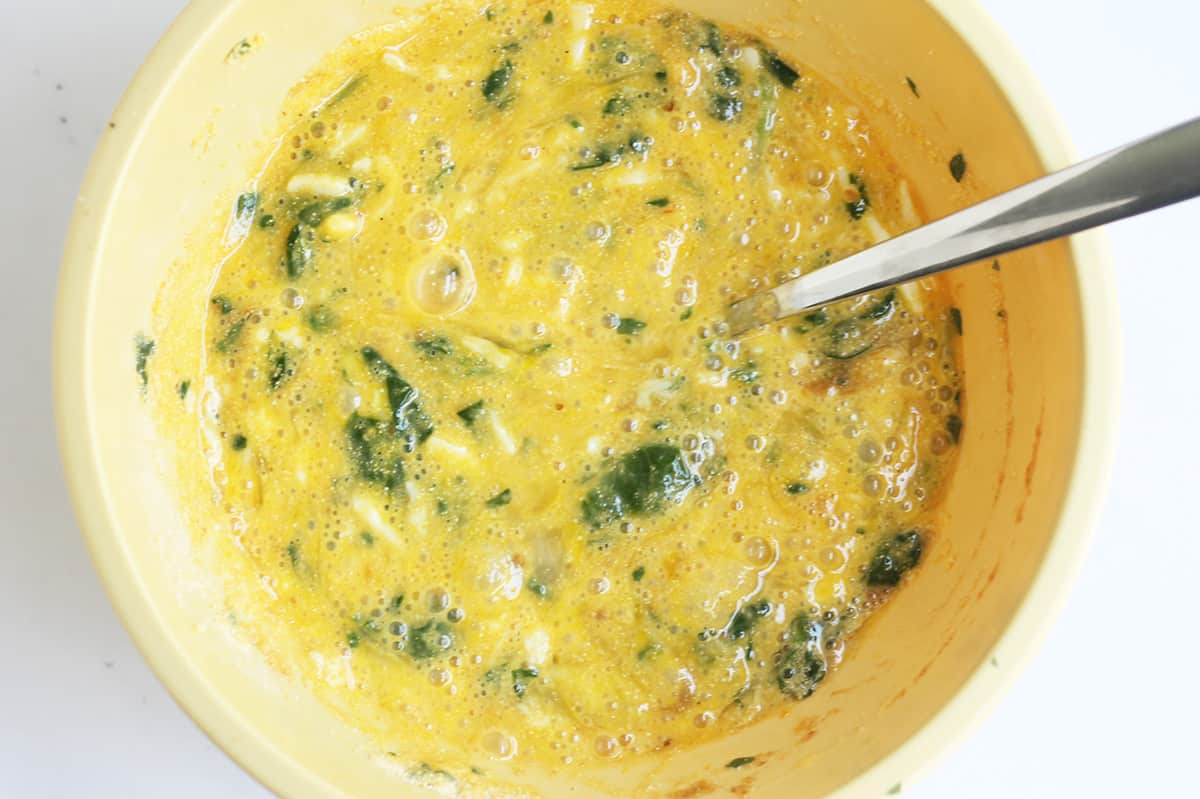 mixing batter for spinach egg muffins in yellow bowl.