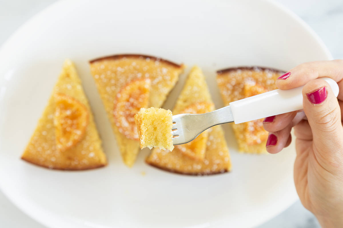 Fork holding olive oil cake piece with slices on plate.