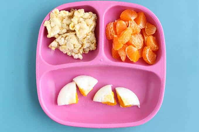 toddler breakfast idea eggs and fruit on pink plate with rice cakes