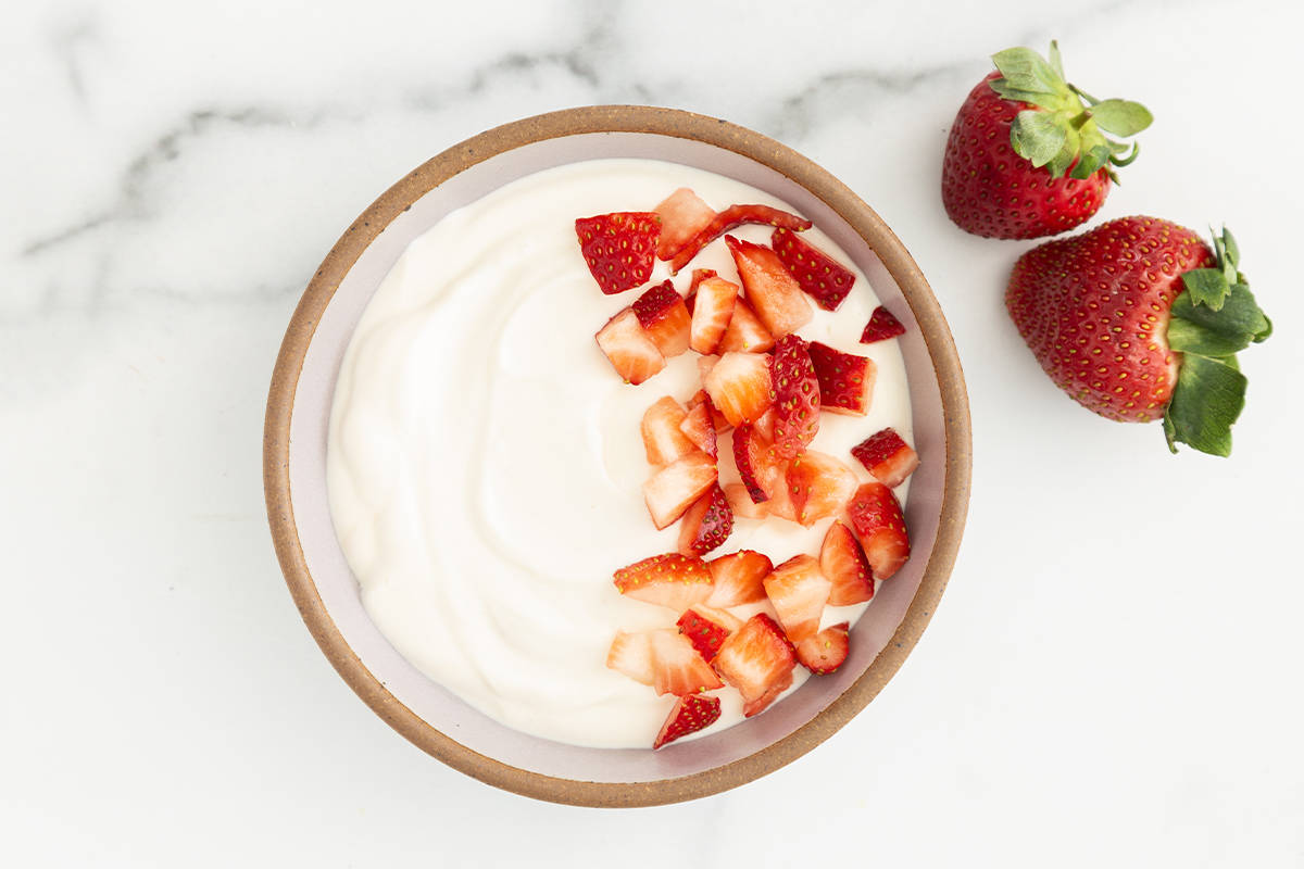 Vanilla yogurt in bowl with strawberries. 